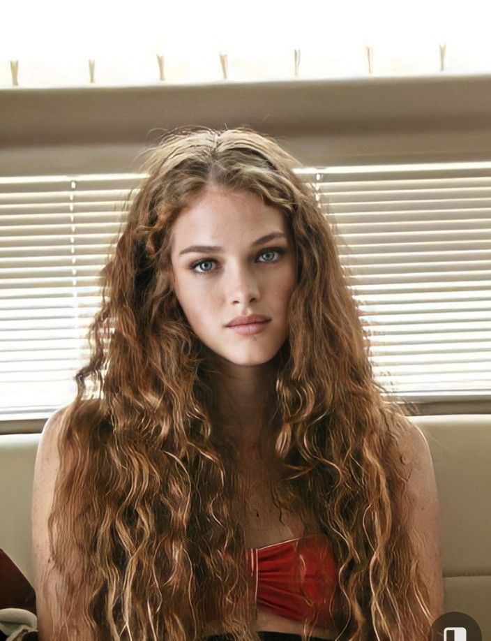 a woman with long curly hair sitting in front of a laptop computer and looking at the camera