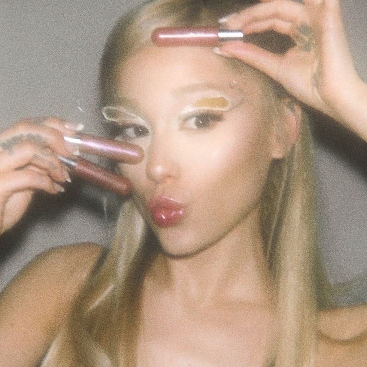 a woman with long blonde hair and makeup holding two glasses in front of her face