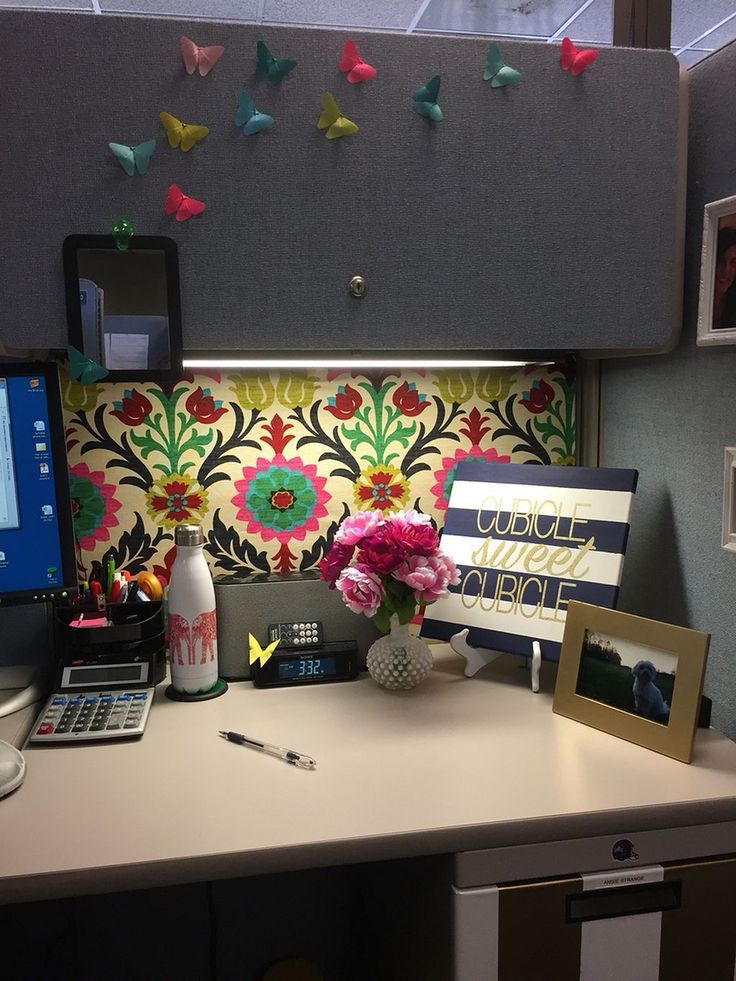 a desk with a laptop, computer monitor and flowers on top of it in an office cubicle