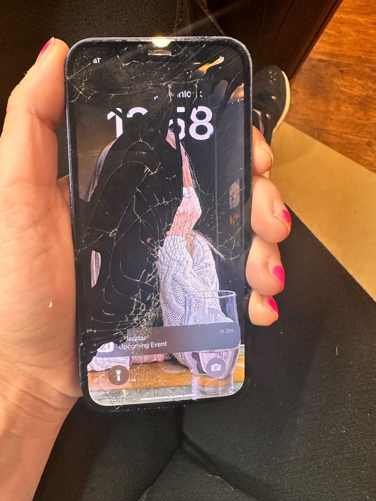 a woman holding up her cell phone with the screen cracked off and showing it's image