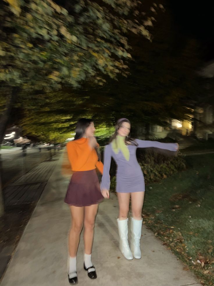 two young women walking down a sidewalk next to each other in short skirts and knee high boots