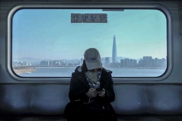 a person sitting on a subway looking at their cell phone with the city in the background