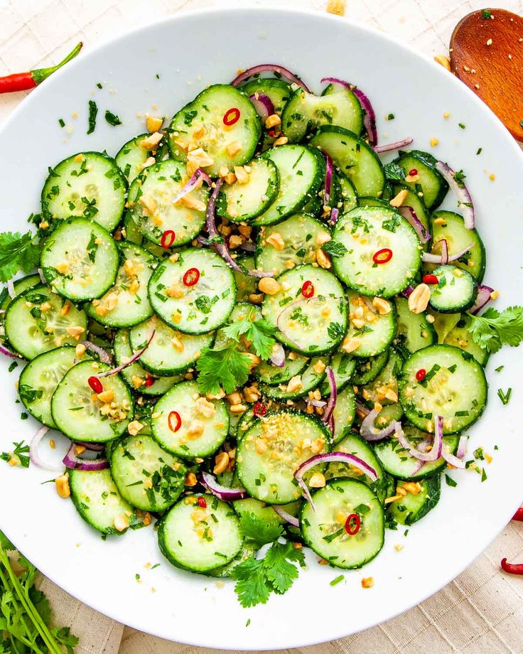 a white bowl filled with cucumbers, onions and cilantro on top of a wooden table