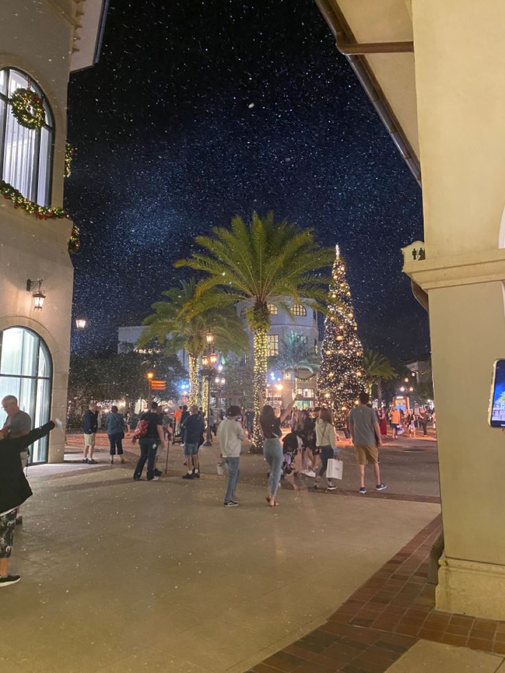 people are standing in the middle of a street at night with christmas trees and lights