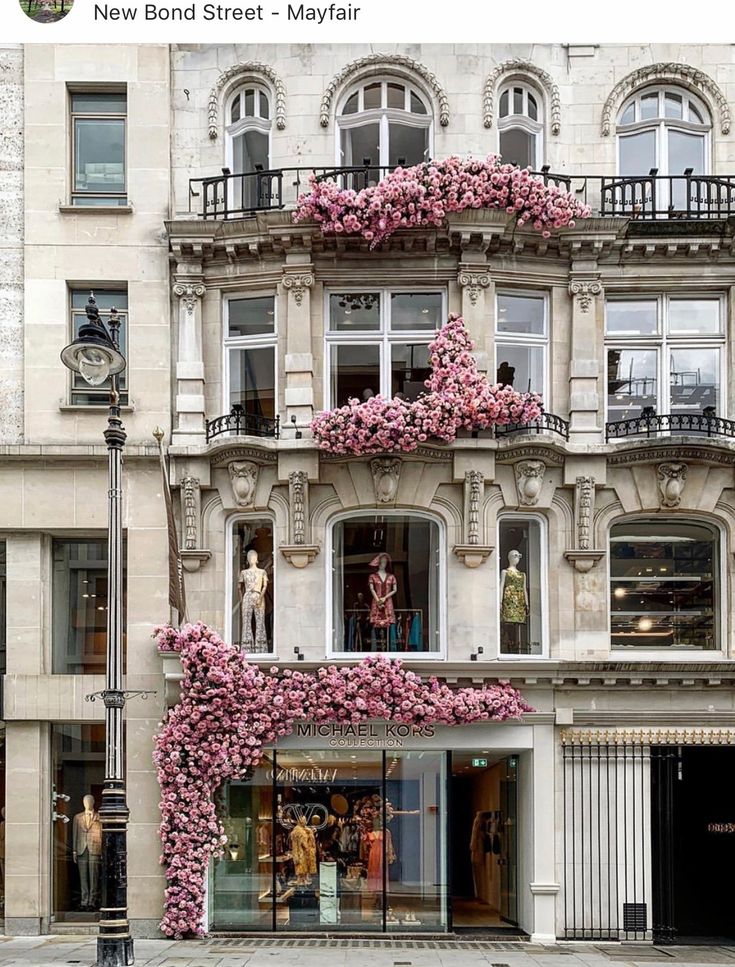 a building with pink flowers growing on the side of it's windows and balconies