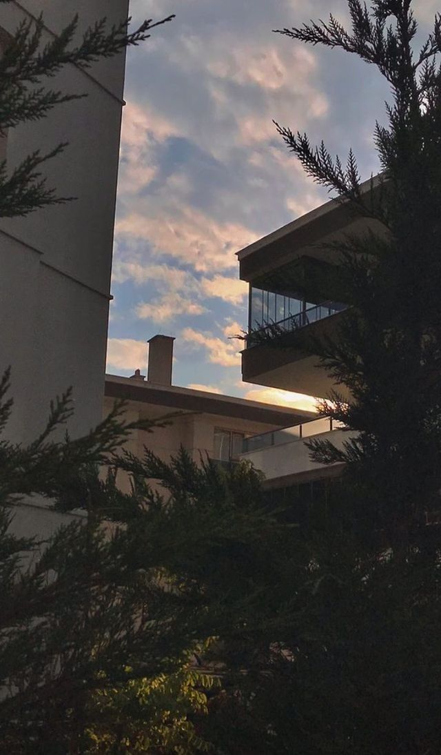 the sun is setting behind some trees in front of an apartment building with balconies