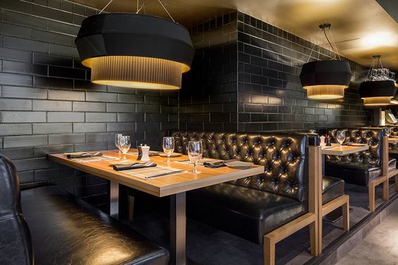 an empty restaurant with black leather booths and gold lighting fixture hanging from the brick wall