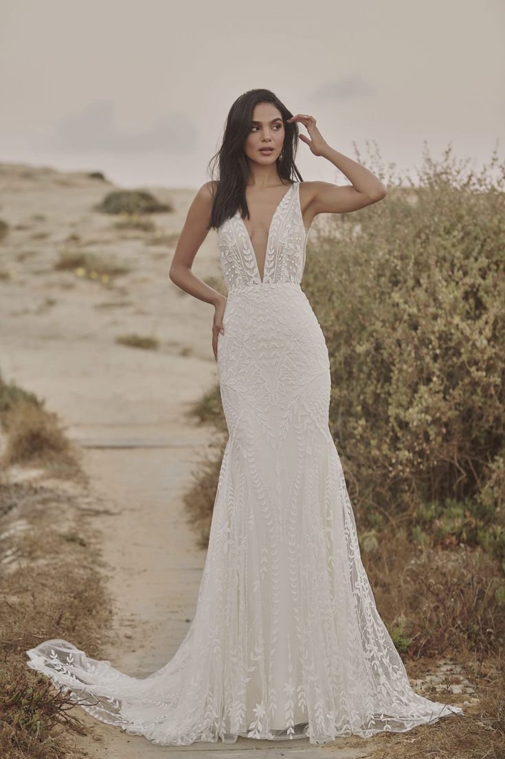 a woman in a white wedding dress standing on a path with her hands behind her head