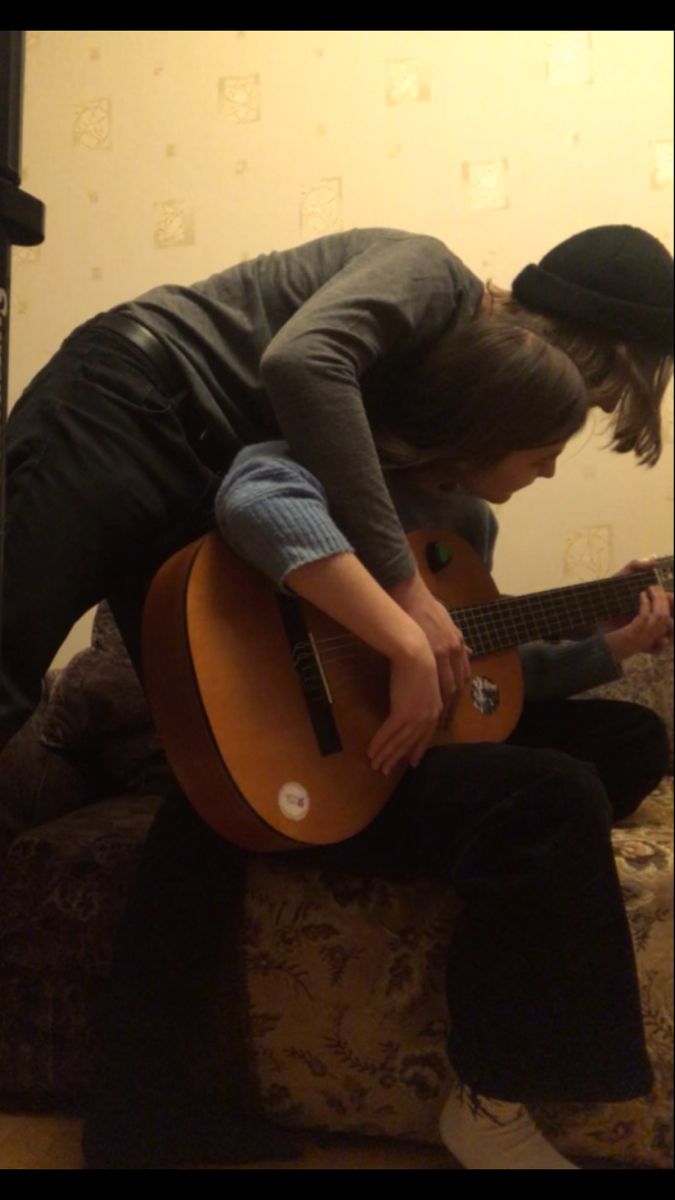 two young men are playing guitars on the couch