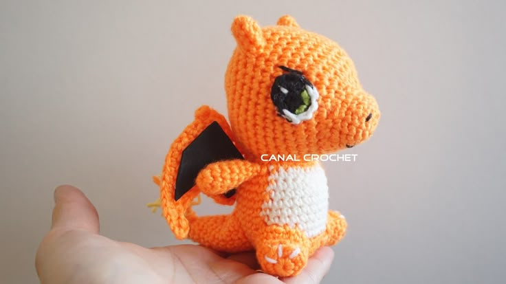 a small crocheted orange and white dragon sitting on top of someone's hand