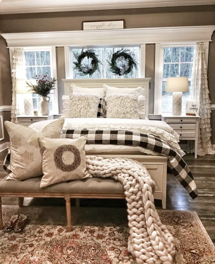 a white bed sitting in a bedroom next to two windows with wreaths on them