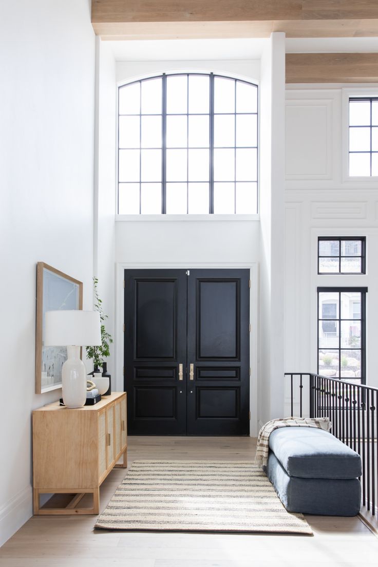 a living room with black doors and white walls, rugs on the floor and a bench in front of it