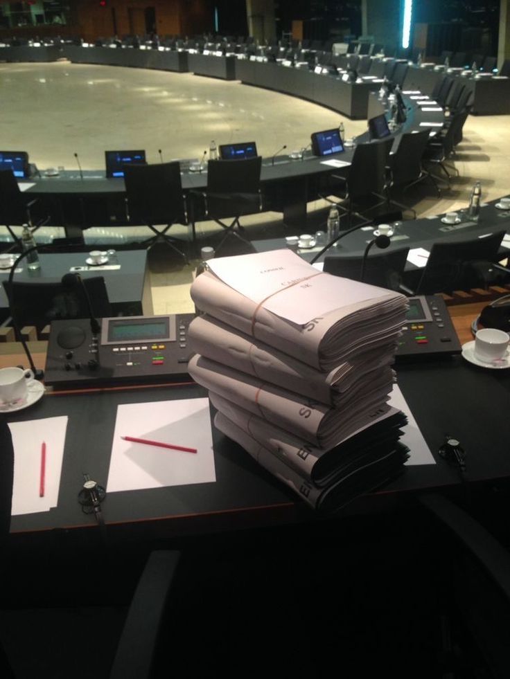 stacks of papers sitting on top of a table in front of a conference room filled with tables and chairs