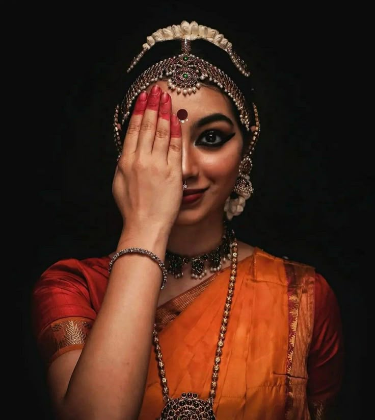 a woman in an orange sari holding her hands up to her face and looking at the camera