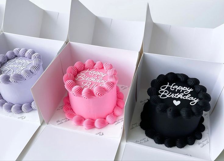 there are three cakes in different boxes on the same table and one is pink, purple, and white