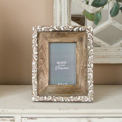 a wooden frame sitting on top of a white dresser next to a potted plant