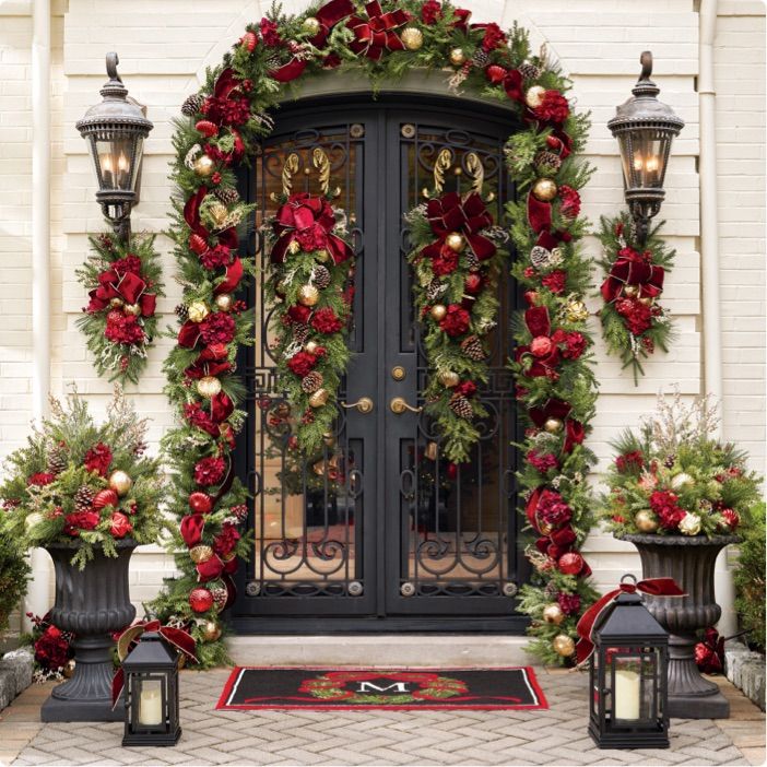 a decorated front door with christmas wreaths and decorations on the outside, along with two lanterns