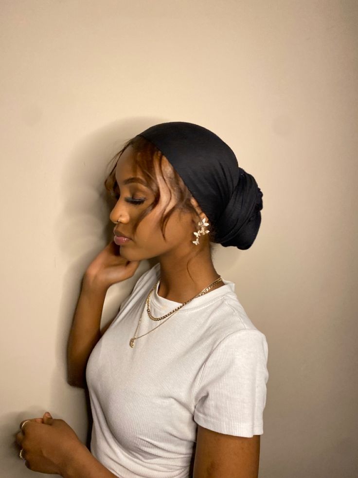 a woman leaning against a wall with her hand on her chin, wearing a white shirt and black turban