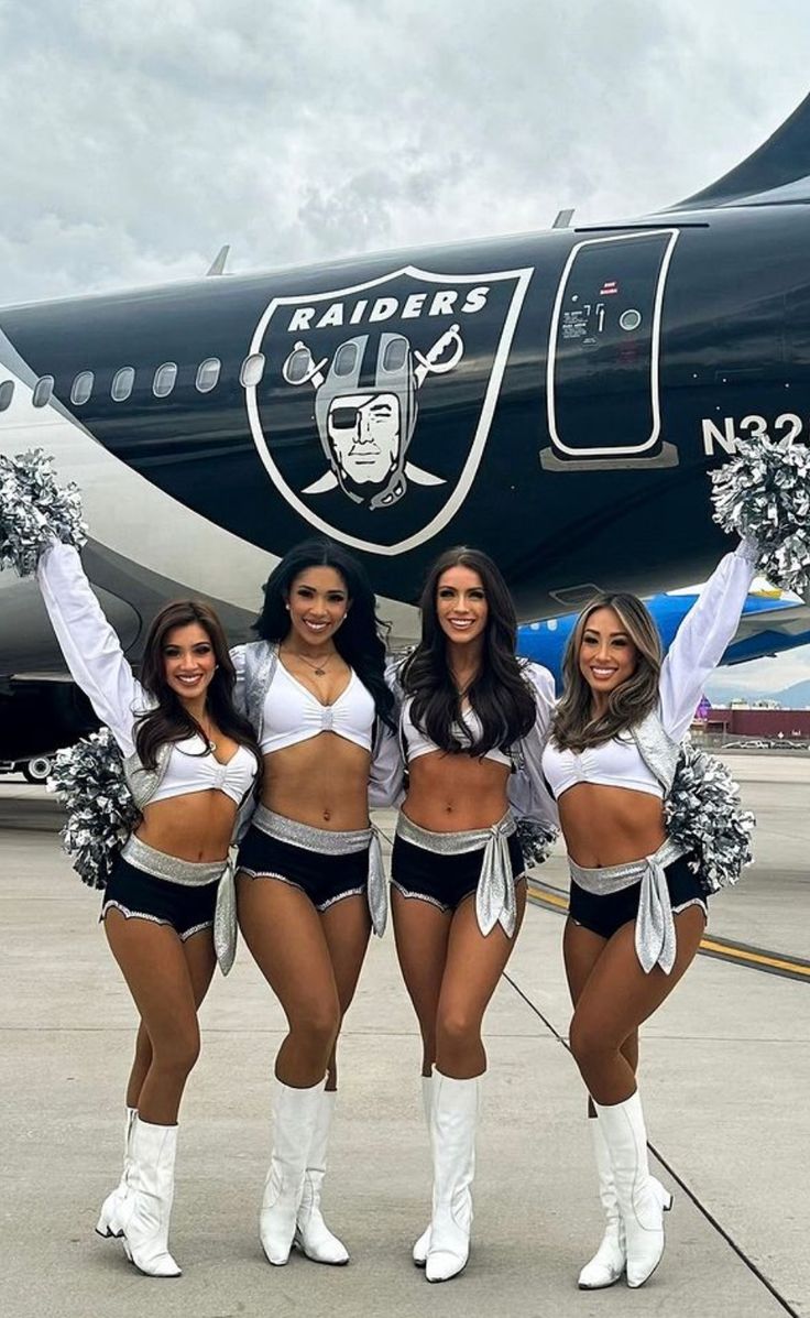 four cheerleaders pose in front of an airplane