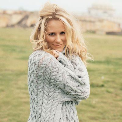 a woman standing in a field wearing a sweater