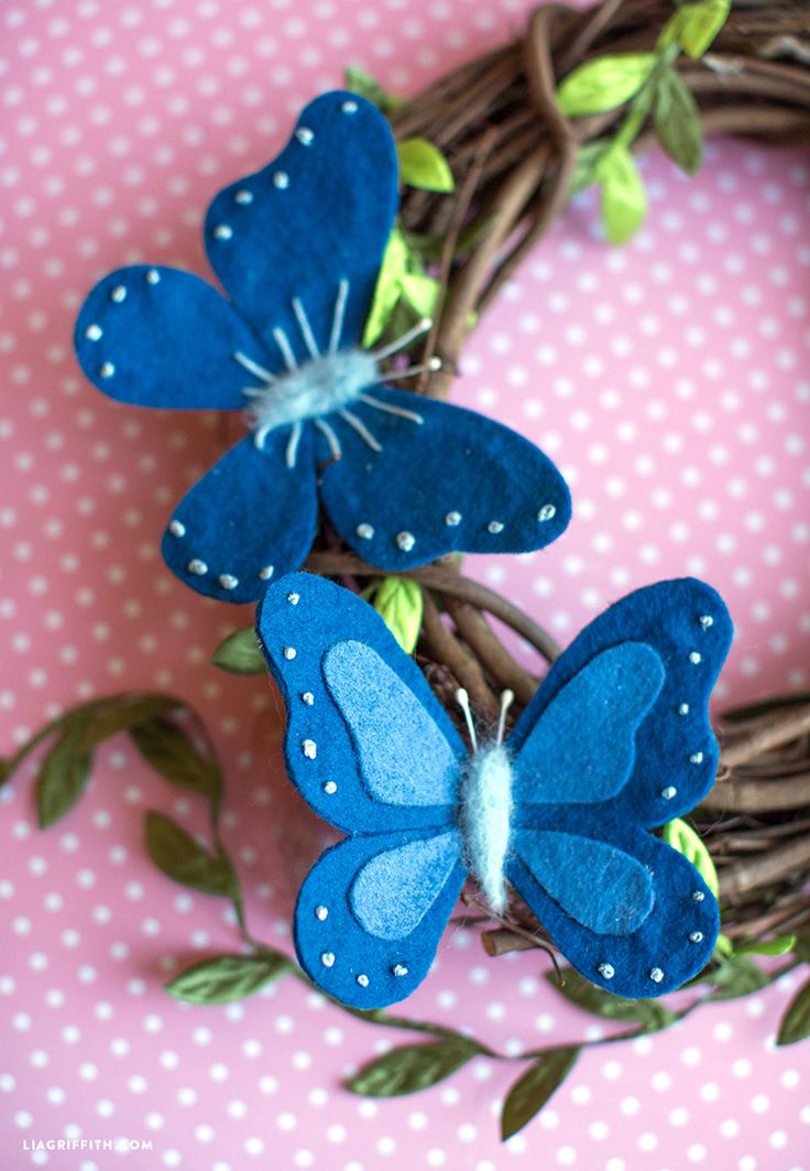 two blue butterflies sitting on top of a twig next to a wreath with green leaves