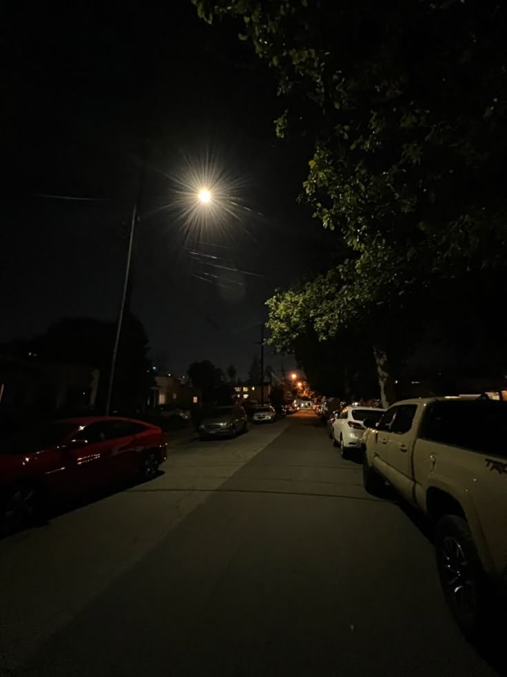 a street at night with cars parked on the side and lights shining in the sky