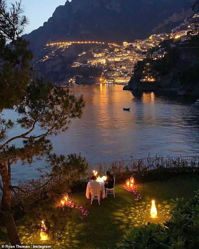 an outdoor dinner is set up on the lawn by the water at night with lit candles