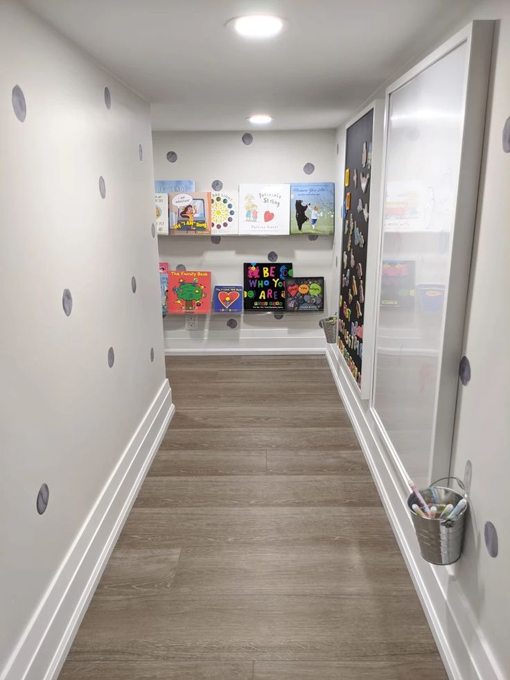 an empty hallway with polka dots on the walls and wooden floors, leading to children's bookshelves