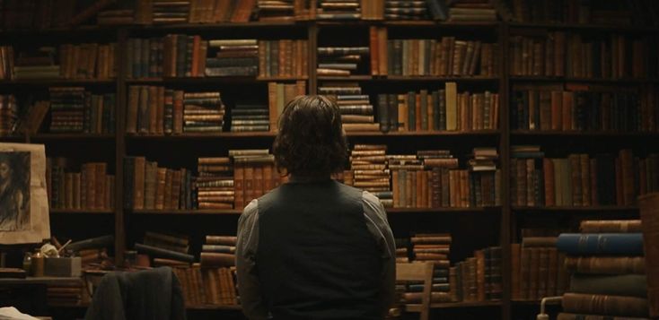 a person sitting in front of a bookshelf full of books and looking into the distance