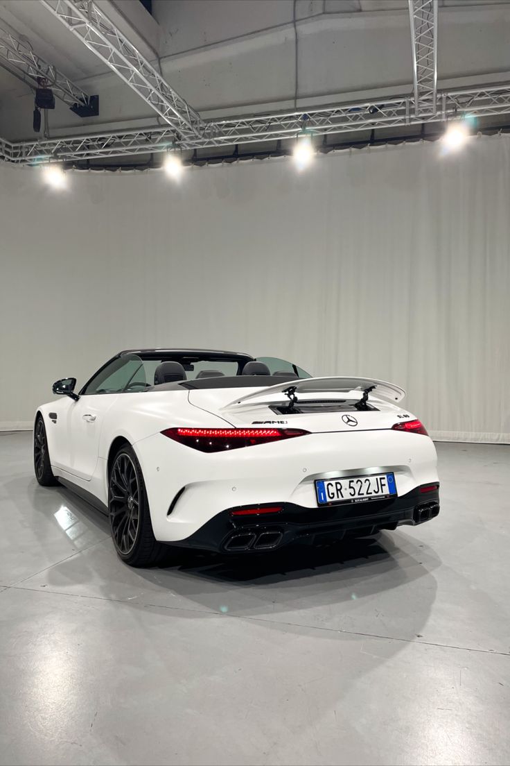 the rear end of a white sports car in a large room with lots of lights