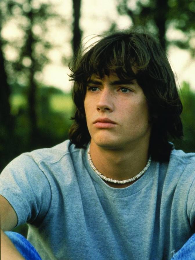 a young man sitting in the grass with his hand on his hip and looking off into the distance