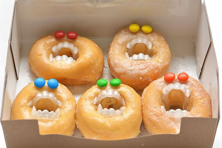 six doughnuts in a box with gummy bears on the top one has eyes and teeth