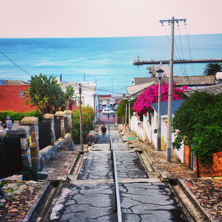 an empty street next to the ocean with people walking on it and houses in the background