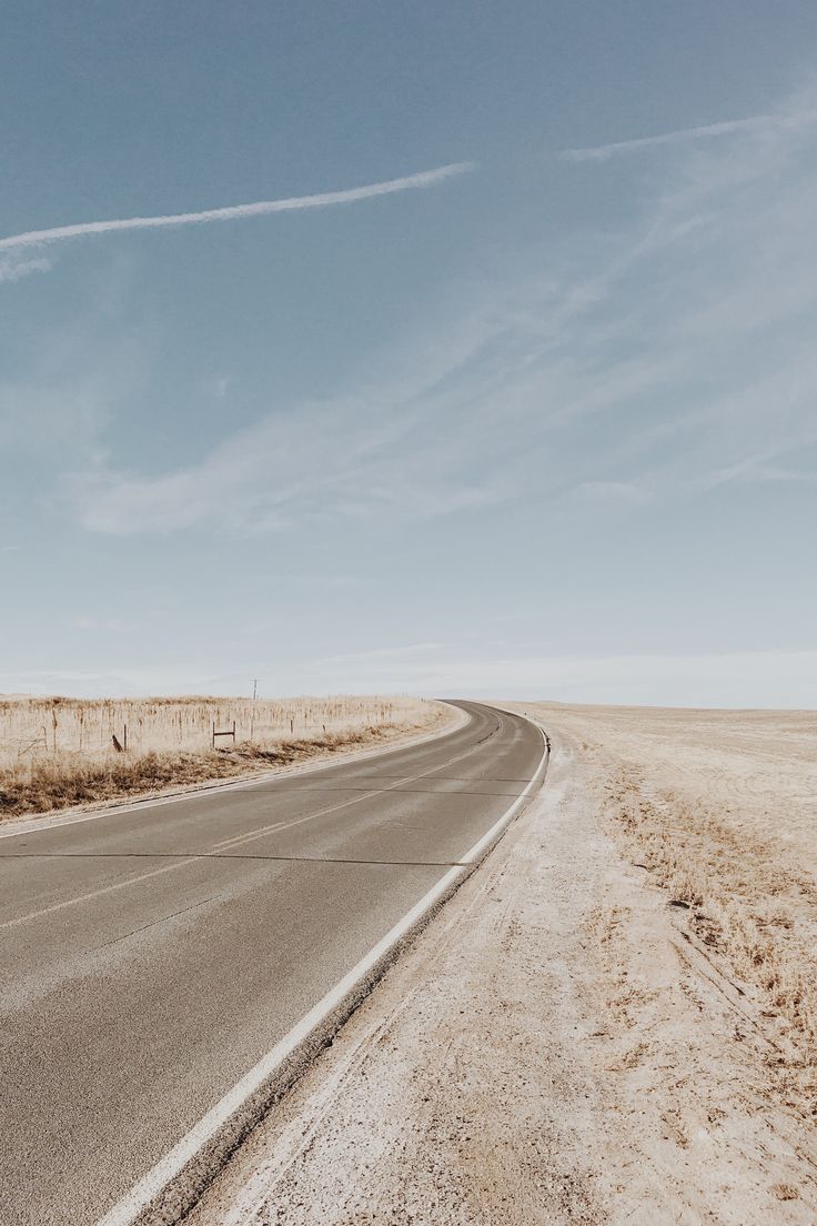 an empty road with no cars on it in the middle of nowhere, under a blue sky