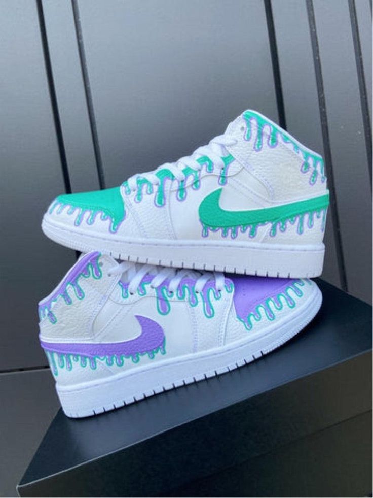 a pair of white and green sneakers on top of a black box with purple drips