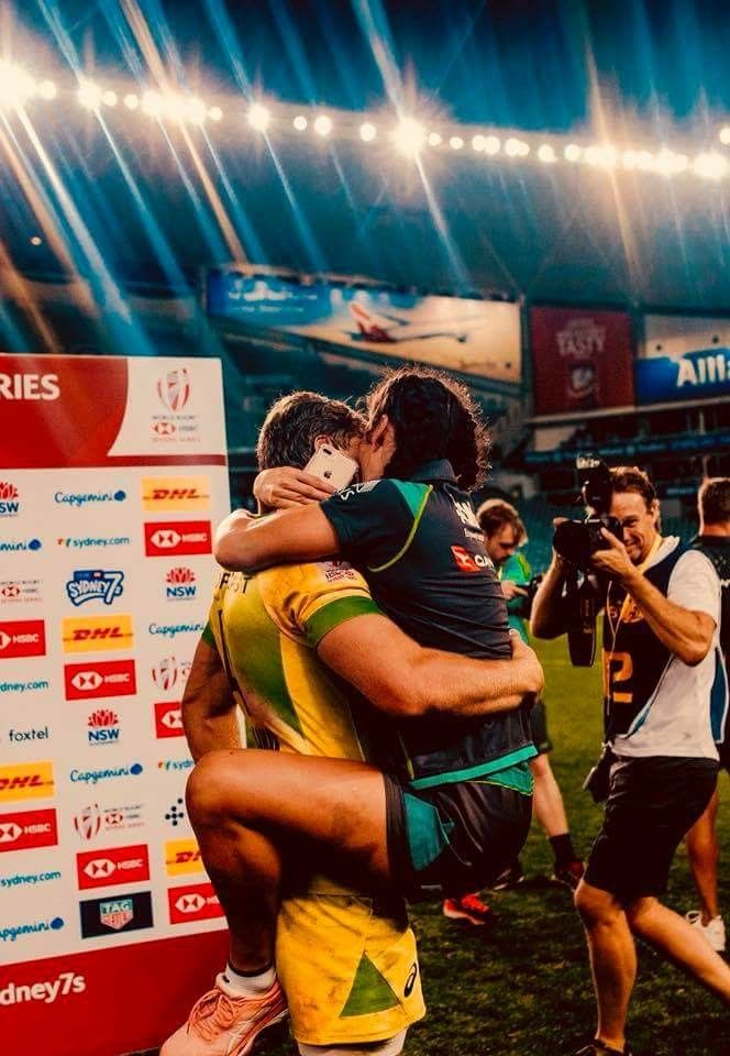 two rugby players hugging each other in front of an audience at a stadium with bright lights