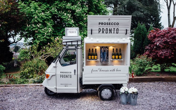 a small food truck parked in front of some trees and bushes with bottles on the back