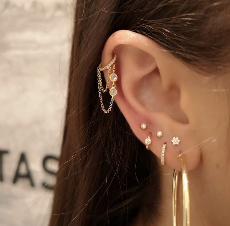 a close up of a person wearing gold ear cuffs and earrings with chains attached to them