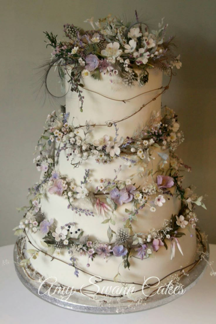 a three tiered wedding cake decorated with flowers and greenery on a silver platter