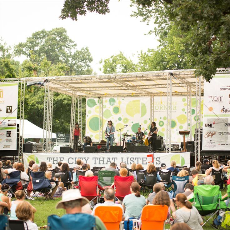 people are sitting in lawn chairs and watching an outdoor music band play on the stage