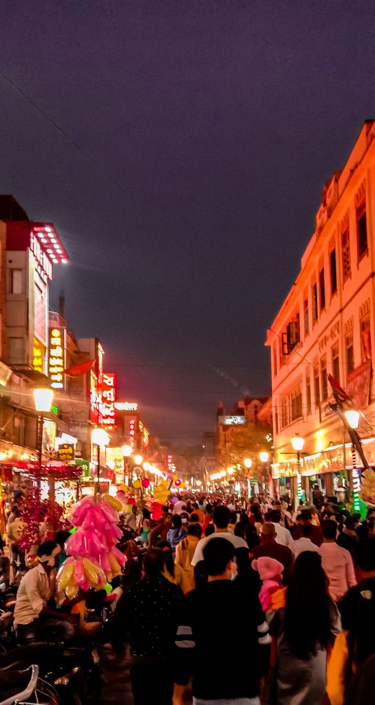 a crowd of people walking down a street next to tall buildings with neon lights on them