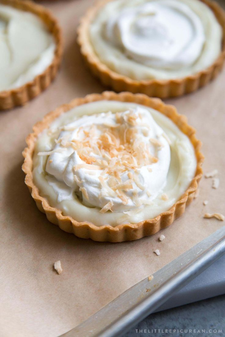 three tarts with whipped cream on top are sitting on a baking sheet next to a knife