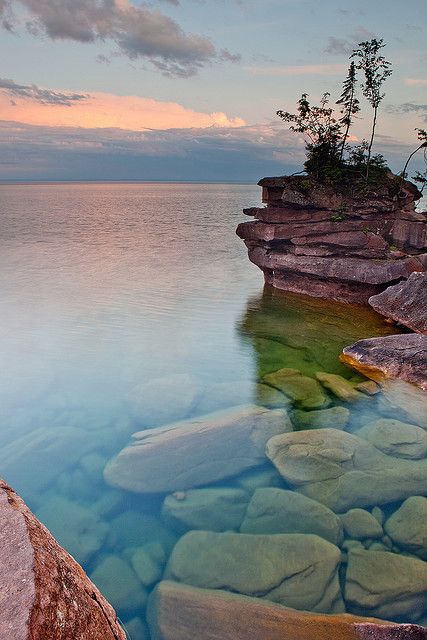 a body of water with rocks and trees in the middle of it at sunset or dawn