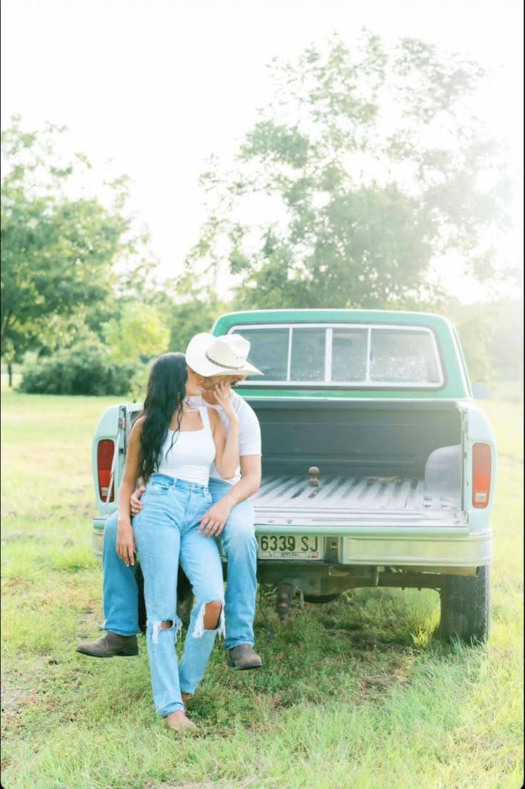 a man and woman sitting on the back of a pick up truck in a field