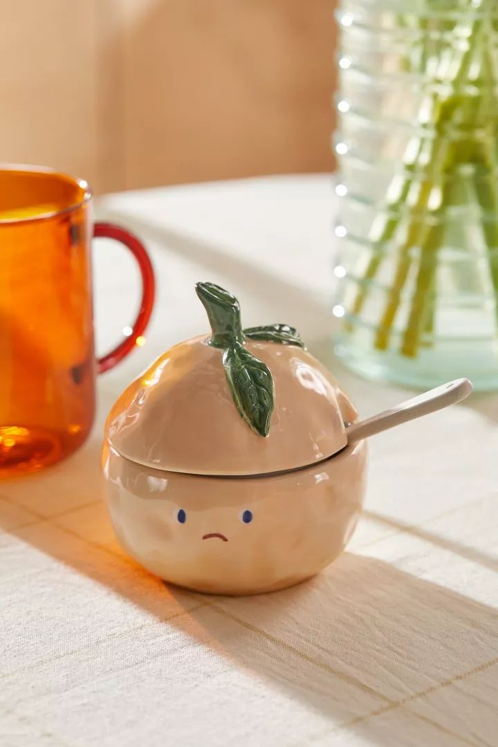 a ceramic fruit with a spoon in it sitting on a table next to a cup