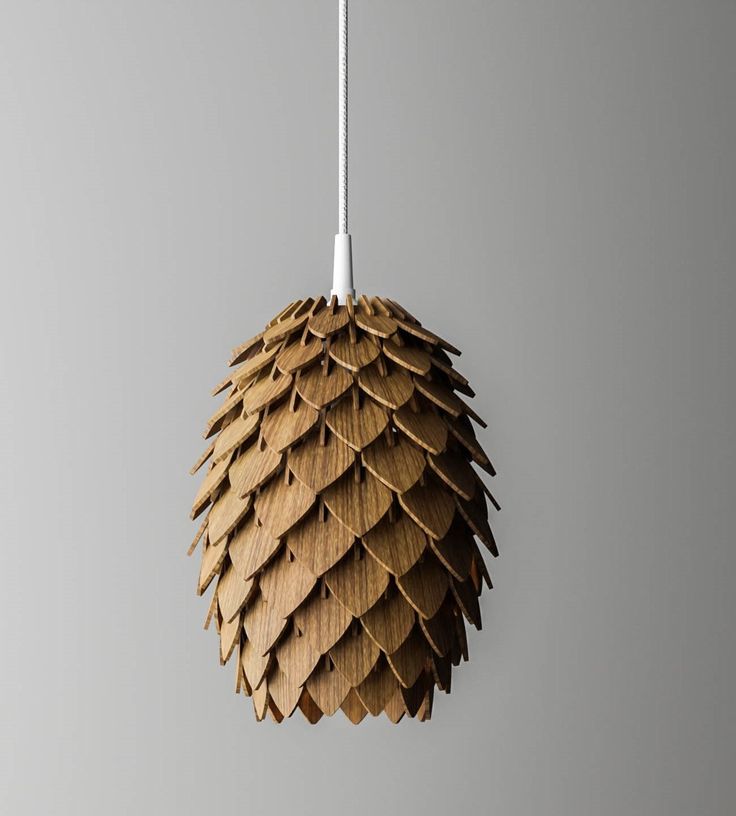 a wooden pine cone hanging from a white cord on a gray wall with a light fixture in the background