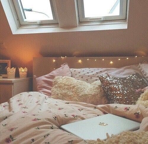 there is a laptop on the bed with pink sheets and lights in the window sill