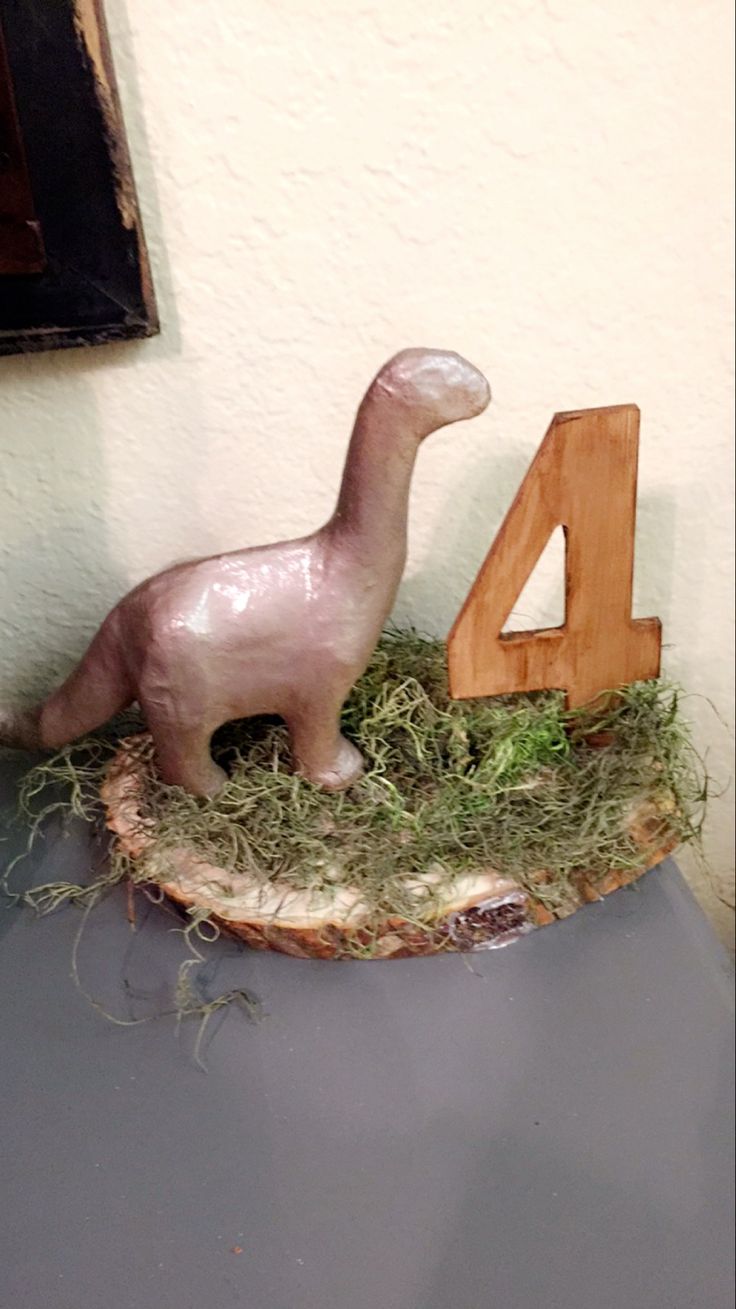 a dinosaur figurine sitting on top of a table next to a number four