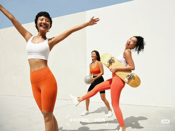 three women in orange and white outfits are holding skateboards while one woman holds her arms out to the side