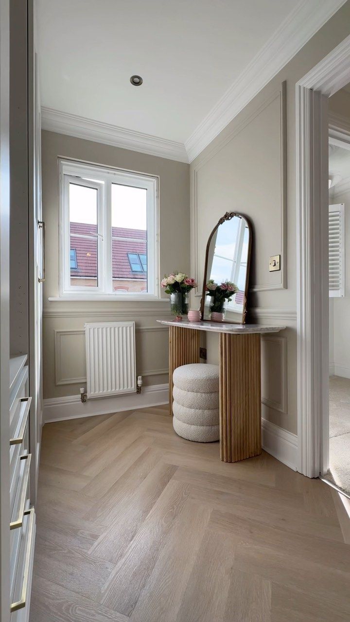 an empty room with a mirror, stool and flower vases on the table in front of it